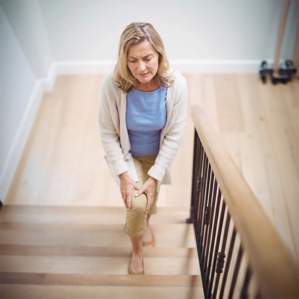 Eine Frau steigt mit Knieschmerzen eine Treppe hinauf.
